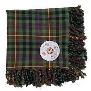 May include: A green, brown, and black plaid scarf with a silver brooch. The scarf has a fringed edge and a pattern of yellow and blue lines. The brooch is round with a central gem and three smaller gems.