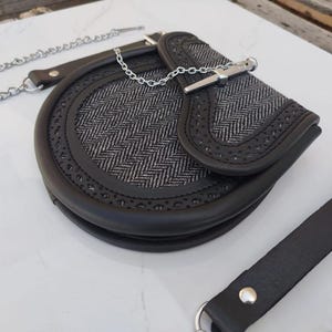 Pu&ograve; includere: Una borsa in pelle nera con una catena argentata e una chiusura argentata. La borsa ha un motivo a spina di pesce e un bordo decorativo.