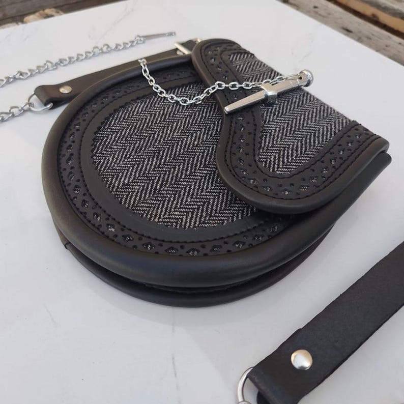 Pu&ograve; includere: Una borsa in pelle nera con una catena argentata e una chiusura argentata. La borsa ha un motivo a spina di pesce e un bordo decorativo.