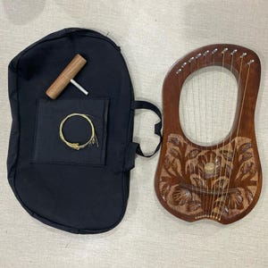 Può includere: Una lira in legno con un design floreale e 15 corde. La lira viene fornita con una custodia di trasporto nera, una chiave di accordatura e un set di corde di ricambio.