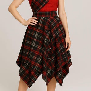 Könnte beinhalten: Ein rot-schwarz karierter Rock mit einem einzigartigen asymmetrischen Saum. Der Rock hat eine Reihe dekorativer Metallverschlüsse auf der Vorderseite und einen passenden roten Bund. Der Stoff hat ein klassisches Tartanmuster.