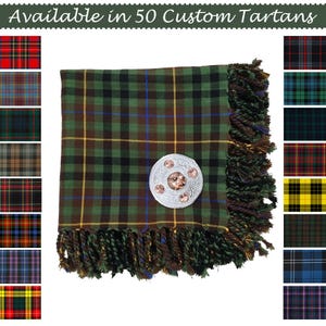 May include: A green, black, and brown tartan scarf with a decorative silver brooch. The scarf has a fringed edge and is displayed with several tartan pattern samples. Text reads "Available in 50 Custom Tartans."