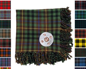 Puede incluir: Bufanda de tartán verde, negro y marrón con un broche decorativo plateado. La bufanda tiene un borde con flecos y se muestra con varias muestras de patrones de tartán. El texto dice "Available in 50 Custom Tartans."