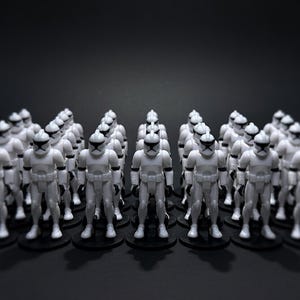 May include: A large group of white action figures, each with a black visor and helmet, stand on black circular bases. The figures are arranged closely together against a dark background, creating a sense of a uniformed army.