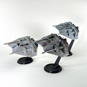 May include: Three miniature gray and red spacecraft models with black stands. The models have detailed features, including wings, turrets, and cockpit windows. The stands are round with a ribbed design.