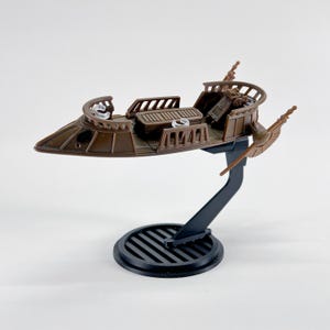 May include: A brown model of a futuristic vehicle, possibly a spacecraft or hovercraft, with a detailed interior and exterior design. The model is mounted on a black stand with a circular base. The vehicle has a sleek, aerodynamic shape.