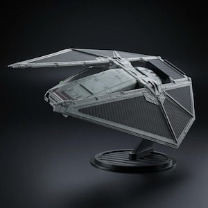 May include: A gray TIE Striker starfighter model featuring angular wings with dark gray paneling and a central cockpit section. The spacecraft is mounted on a circular black display stand, showcasing its aerodynamic design and detailed surface plating.