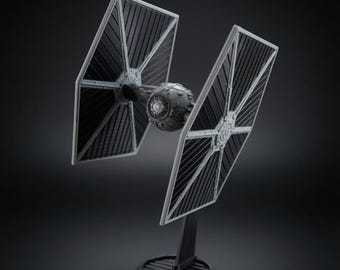 May include: A gray and black TIE fighter model spacecraft featuring a spherical central cockpit pod flanked by two large, flat, hexagonal solar array wings. The detailed miniature vehicle is mounted on a black circular display stand base.