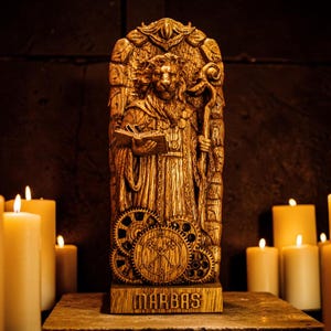 May include: A golden-colored statue of a robed figure holding a book and staff, with a gear-themed design at the base. The statue is labeled "MARBAS" and is surrounded by lit candles, creating a warm, mystical ambiance.
