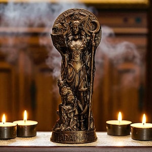 May include: A bronze-colored statue of a woman holding a book and staff, with a wolf at her feet. The statue is surrounded by smoke and four lit tea light candles. The statue is on a wooden table.