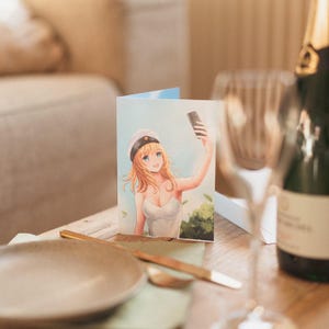 May include: A card featuring an illustration of a woman with blonde hair wearing a blue and white sailor hat taking a selfie with a smartphone. The woman is wearing a white tank top and is standing in front of a green background.