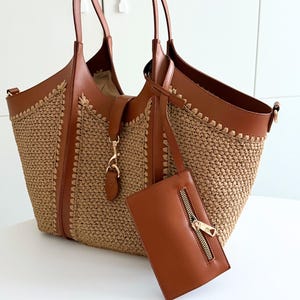 May include: A brown tote bag with a woven straw body and leather trim. The bag has two handles and a detachable small pouch with a zipper. The bag is open, revealing the interior.