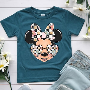 Puede incluir: Una camiseta de manga corta color verde azulado oscuro con un gr&aacute;fico de una cabeza de rat&oacute;n de dibujos animados que lleva gafas en forma de coraz&oacute;n y un lazo. El lazo y las gafas tienen un patr&oacute;n de tablero de ajedrez blanco y negro.