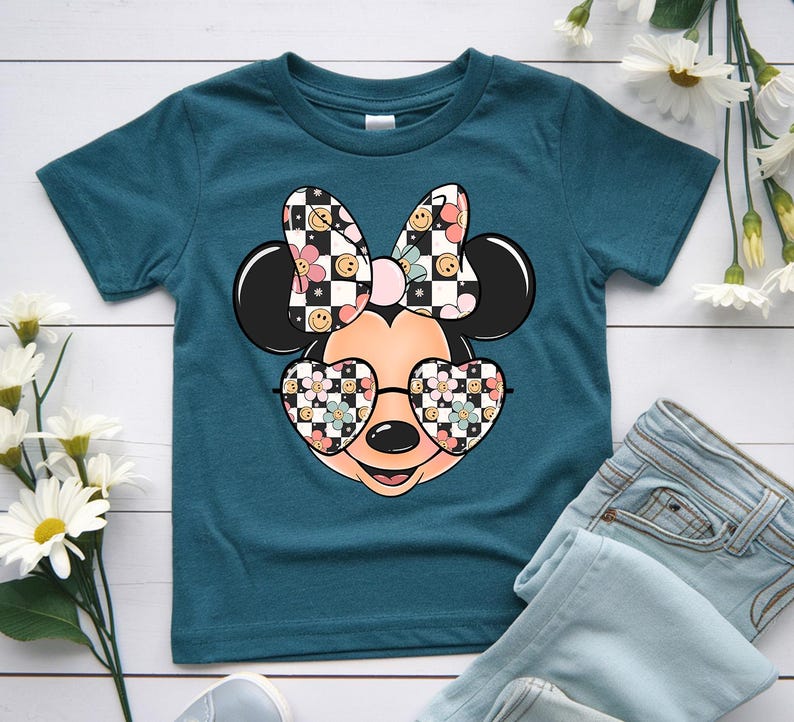 Puede incluir: Una camiseta de manga corta color verde azulado oscuro con un gr&aacute;fico de una cabeza de rat&oacute;n de dibujos animados que lleva gafas en forma de coraz&oacute;n y un lazo. El lazo y las gafas tienen un patr&oacute;n de tablero de ajedrez blanco y negro.