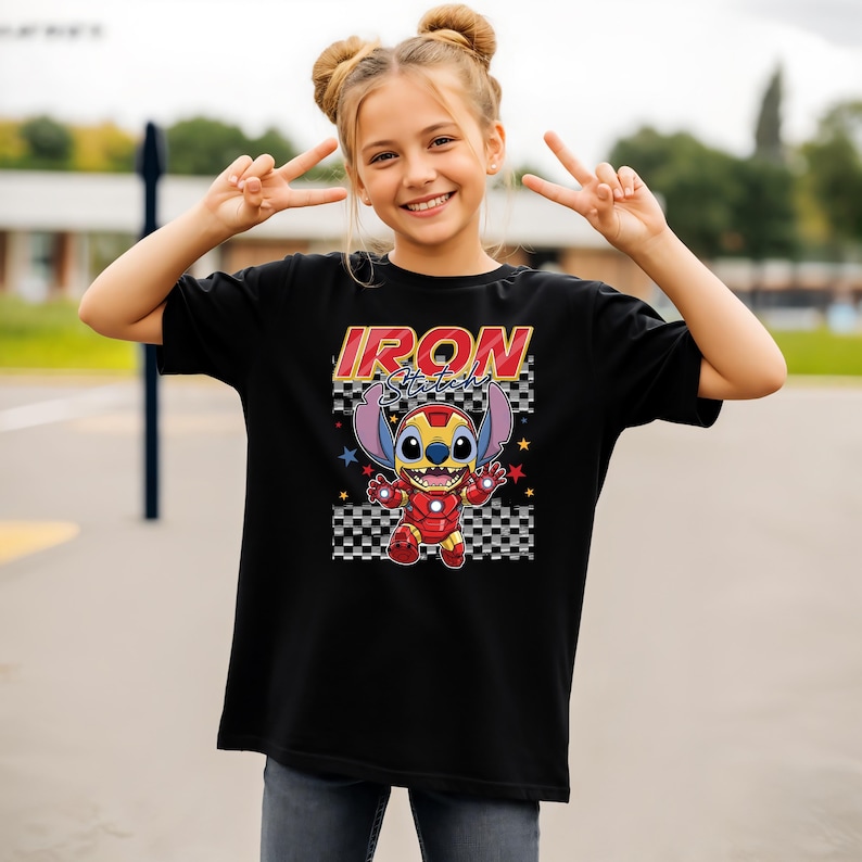 May include: Black t-shirt featuring a cartoon character in an Iron Man suit with the text "Iron Stitch" in red and yellow. The design includes stars and a checkered pattern. The shirt is a casual wear item.