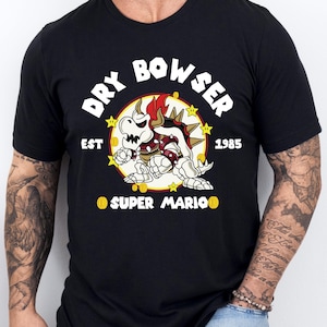 May include: Black t-shirt featuring a graphic of Dry Bowser from Super Mario. The design includes the text "DRY BOWSER" above the character, with "EST 1985" and "SUPER MARIO" below. The character is in red, white, and yellow.