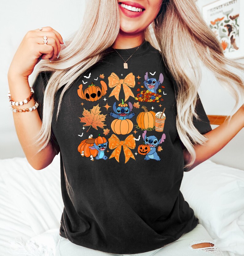 Puede incluir: Camiseta negra con un dise&ntilde;o colorido de Halloween. El dise&ntilde;o incluye calabazas, lazos naranjas, hojas de oto&ntilde;o y un personaje de dibujos animados azul. La camiseta es de estilo casual.