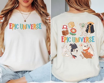 May include: Cream-colored t-shirt with the text "EPIC UNIVERSE" in colorful, dripping letters. The back of the shirt features various cartoon graphics, including a mushroom, a mummy, a dragon, and an owl.
