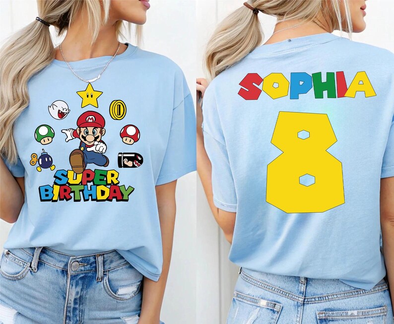 K&ouml;nnte beinhalten: Hellblaues T-Shirt mit einer Grafik eines Videospielcharakters und dem Schriftzug "SUPER BIRTHDAY". Auf der R&uuml;ckseite des Shirts stehen der Name "SOPHIA" und die Zahl "8" in Gelb.