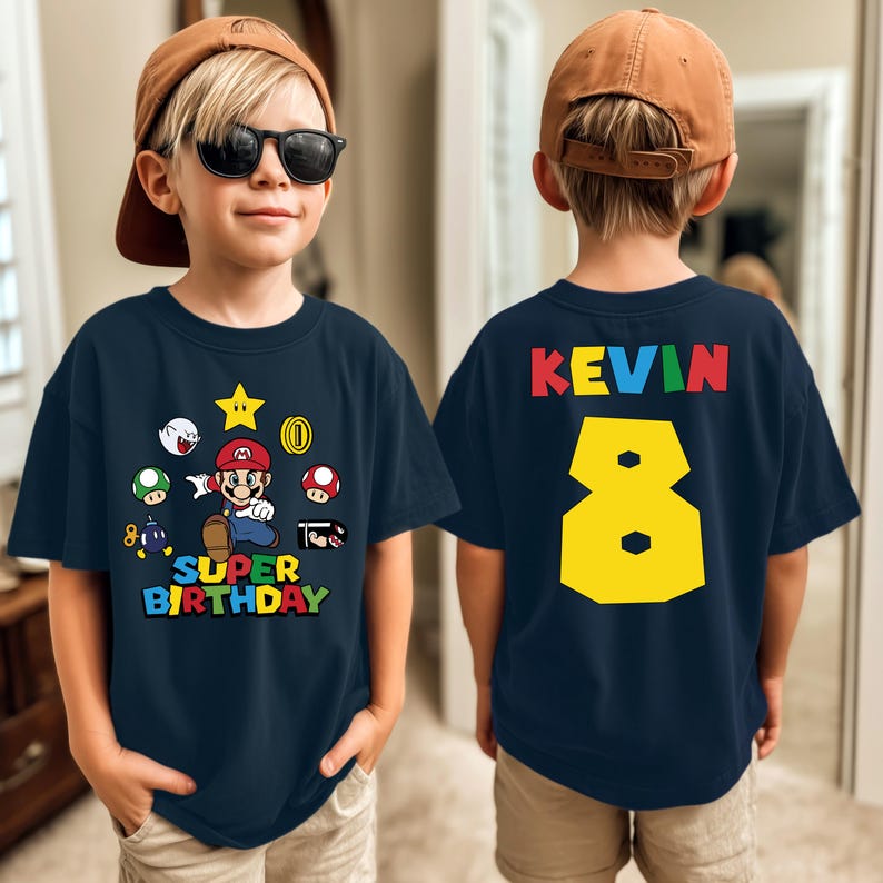K&ouml;nnte beinhalten: Marineblaues T-Shirt mit einem Super Mario-Design, dem Text "SUPER BIRTHDAY" und der Zahl 8. Auf der R&uuml;ckseite des Shirts stehen der Name "KEVIN" und die gelbe Zahl 8.