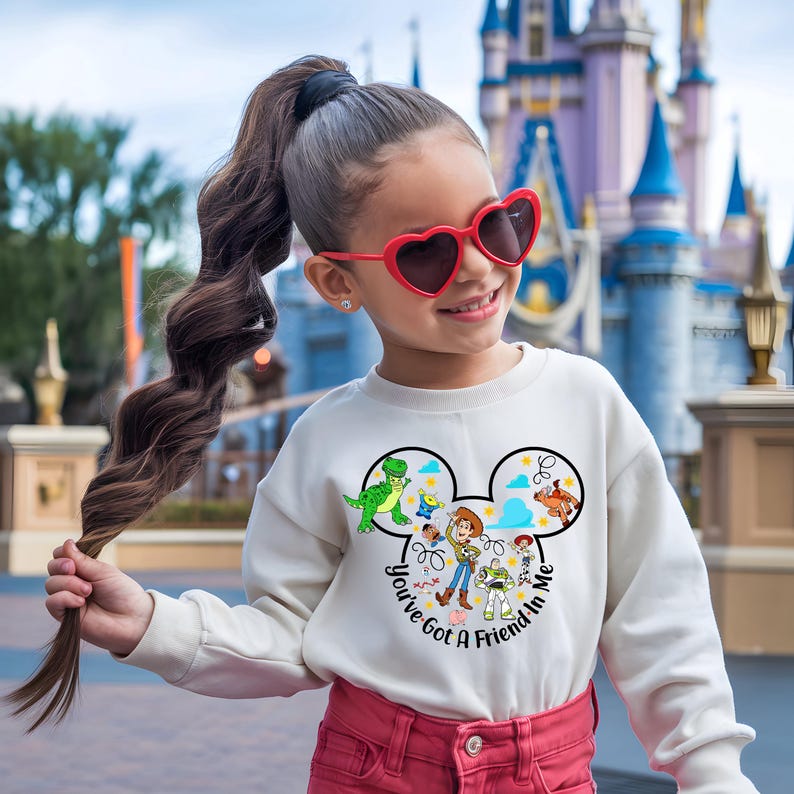May include: A cream-colored sweatshirt featuring a Mickey Mouse head design with characters from the movie Toy Story. The text "You've Got A Friend In Me" is printed on the sweatshirt. The person is wearing red heart-shaped sunglasses.