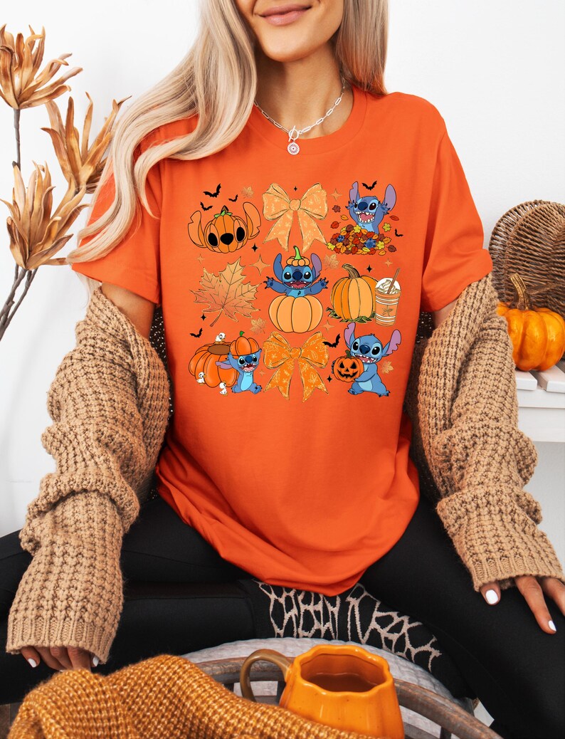 Puede incluir: Camiseta naranja con un dise&ntilde;o de Halloween que presenta personajes de dibujos animados, calabazas y hojas de oto&ntilde;o. La camiseta tiene cuello redondo y mangas cortas. El dise&ntilde;o incluye gr&aacute;ficos relacionados con Halloween en naranja, azul y marr&oacute;n.