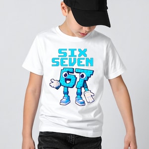 May include: White t-shirt featuring the text "SIX SEVEN" in blue pixelated letters. Below the text are the numbers 6 and 7, designed as cartoon characters with arms, legs, shoes, and gloves. The shirt is worn by a person wearing a black cap.