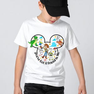 May include: White t-shirt featuring a black Mickey Mouse head design with Toy Story characters. The shirt includes the text "You've Got a Friend in Me" in a circular font. The design showcases characters like Woody, Buzz Lightyear, and Rex.