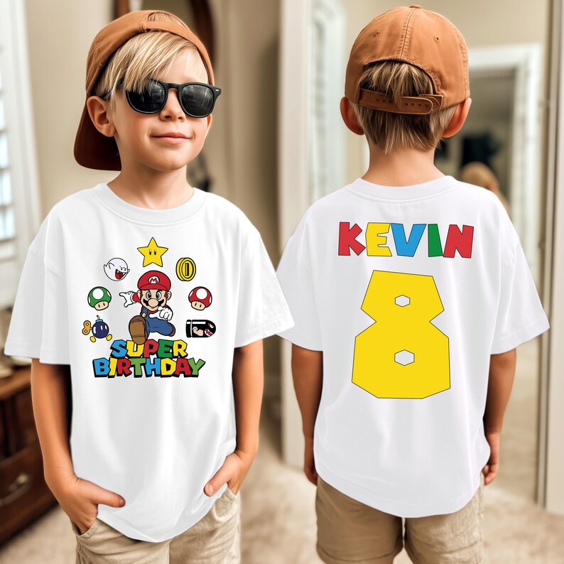 K&ouml;nnte beinhalten: Wei&szlig;es T-Shirt mit einem Super Mario-Design und dem Text "SUPER BIRTHDAY". Auf der R&uuml;ckseite des Shirts stehen der Name "KEVIN" und die Zahl "8" in Gelb. Das Shirt wird von einem Kind getragen.