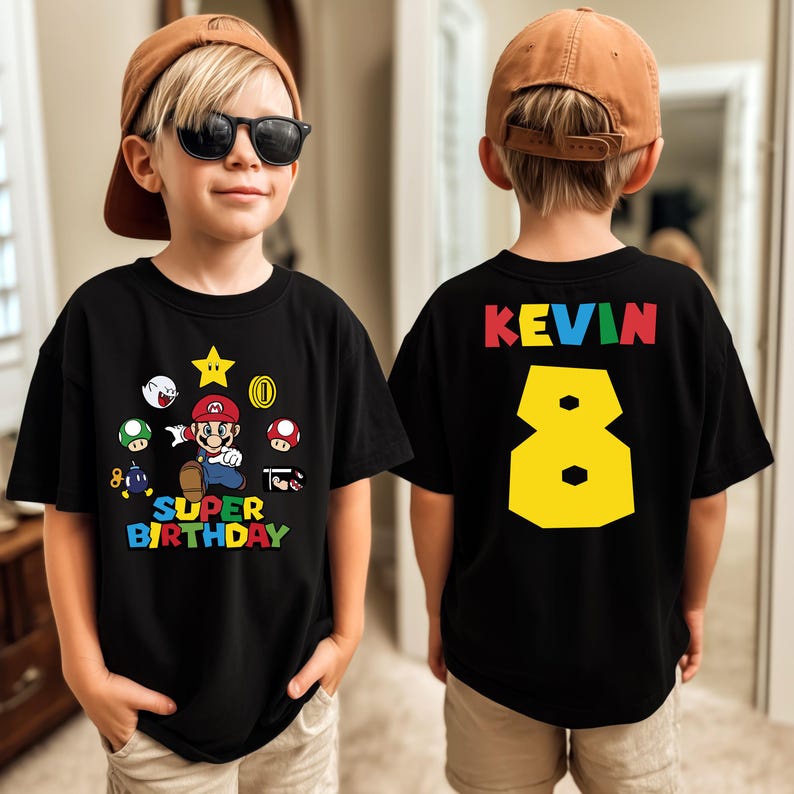 K&ouml;nnte beinhalten: Schwarzes T-Shirt mit einem Super Mario-Motiv und dem Text "SUPER BIRTHDAY". Auf der R&uuml;ckseite stehen der Name "KEVIN" und die gelbe Zahl "8". Das Kind tr&auml;gt eine braune Baseballkappe und eine Sonnenbrille. F&uuml;r den 8. Geburtstag.