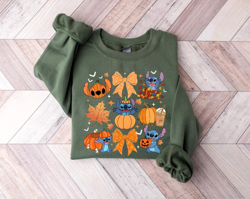 Puede incluir: Una sudadera verde oliva con un dise&ntilde;o tem&aacute;tico de oto&ntilde;o. El dise&ntilde;o incluye personajes de dibujos animados, calabazas, lazos naranjas y hojas de oto&ntilde;o. El gr&aacute;fico est&aacute; centrado en la parte delantera de la sudadera.
