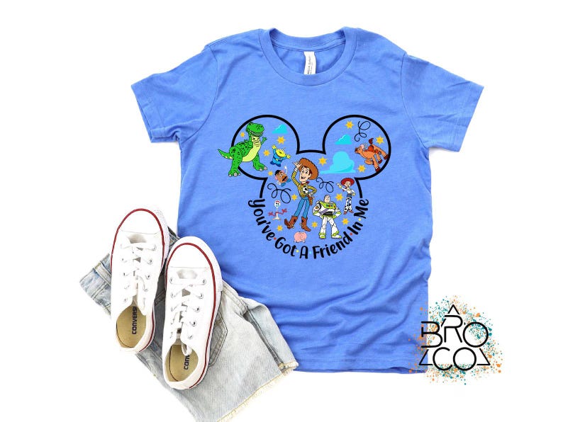 May include: A light blue t-shirt featuring a graphic of Disney's Toy Story characters within a Mickey Mouse ear design. The text "You've Got a Friend in Me" is also included. White sneakers and denim shorts are also in the image.