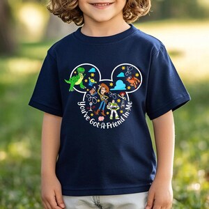 May include: Navy blue t-shirt featuring a graphic of Disney's Toy Story characters within a Mickey Mouse head outline. The design includes Woody, Buzz Lightyear, and other characters, with the text "You've Got A Friend In Me."