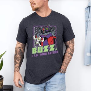 Puede incluir: Camiseta gris oscuro con un gr&aacute;fico de Buzz Lightyear y Zurg con el texto "BUZZ, I AM YOUR FATHER." El dise&ntilde;o incluye acentos morados, rojos y verdes. La camiseta es de manga corta.