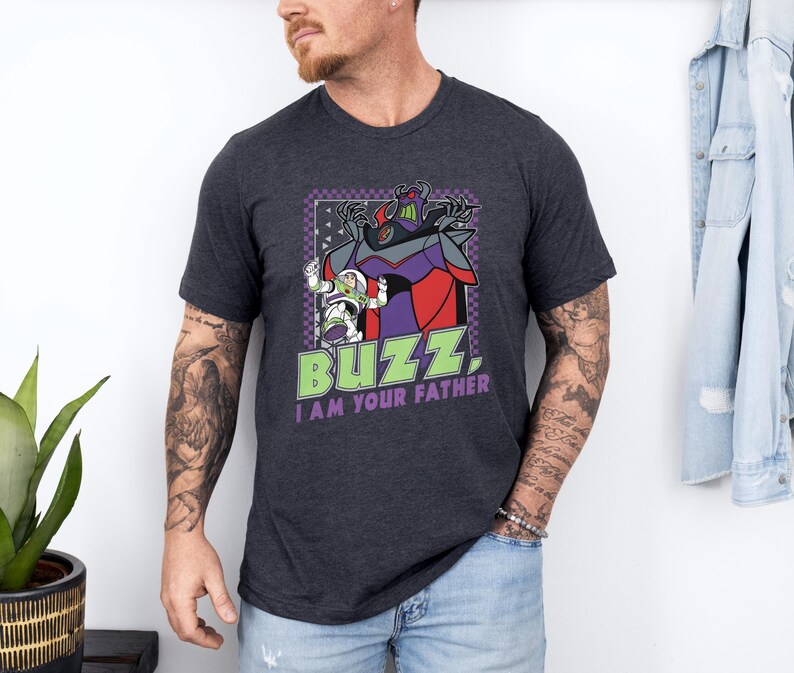 Puede incluir: Camiseta gris oscuro con un gr&aacute;fico de Buzz Lightyear y Zurg con el texto "BUZZ, I AM YOUR FATHER." El dise&ntilde;o incluye acentos morados, rojos y verdes. La camiseta es de manga corta.