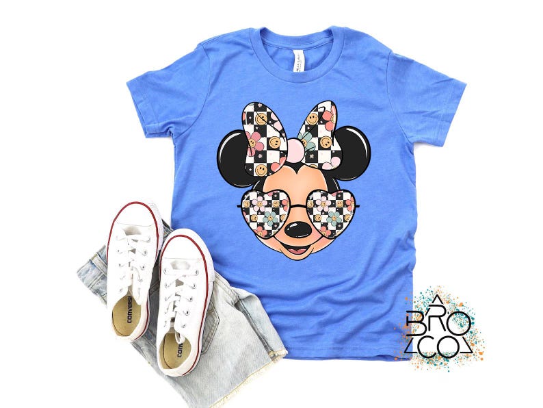 Puede incluir: Una camiseta de manga corta azul claro con un gr&aacute;fico de una cabeza de rat&oacute;n de dibujos animados que lleva gafas en forma de coraz&oacute;n y un lazo. El lazo y las gafas est&aacute;n decorados con un patr&oacute;n de tablero de ajedrez, flores y caras sonrientes.