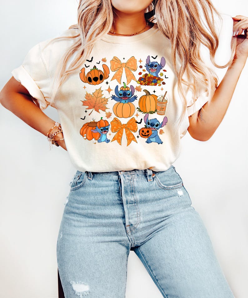 Puede incluir: Camiseta color crema con un dise&ntilde;o tem&aacute;tico de Halloween. El dise&ntilde;o incluye personajes de dibujos animados, calabazas, hojas de oto&ntilde;o y lazos naranjas. La camiseta se combina con vaqueros azul claro.