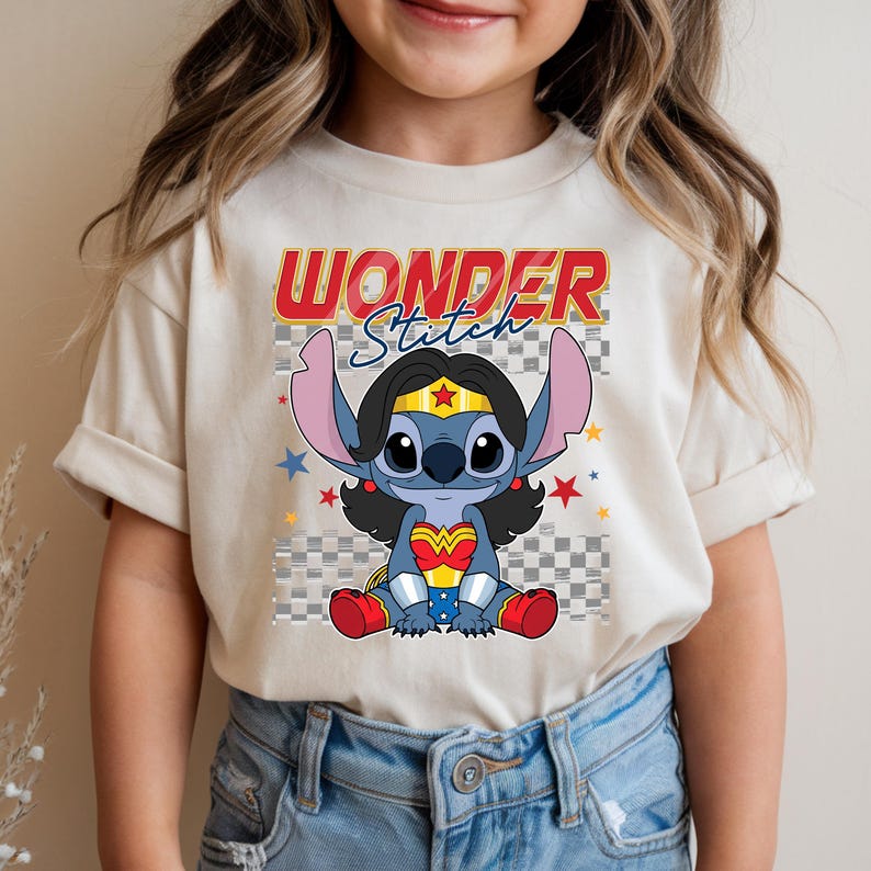May include: Beige t-shirt featuring a cartoon Stitch character dressed as Wonder Woman. The design includes the text "WONDER Stitch" in red and blue, with stars and a checkered background. The character is wearing a gold tiara and red boots.