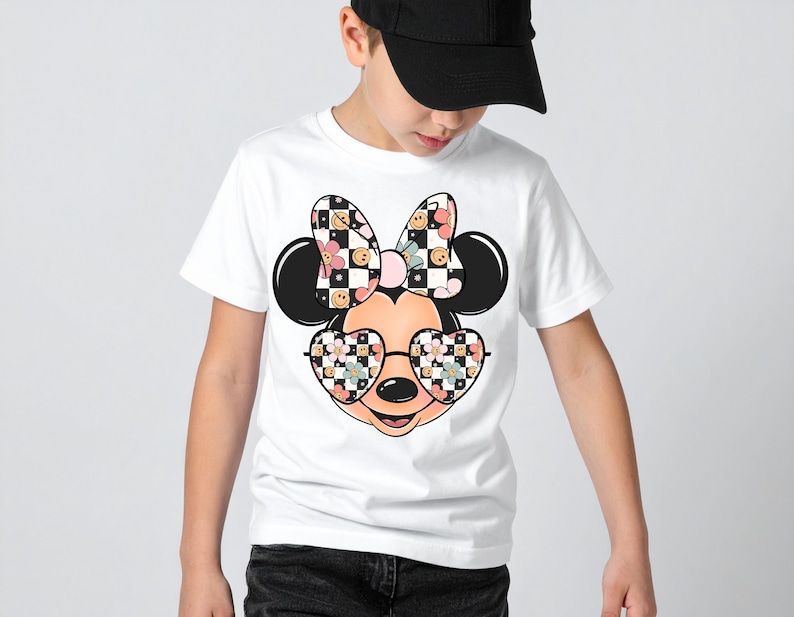 Puede incluir: Una camiseta blanca de manga corta con un gr&aacute;fico de una cabeza de rat&oacute;n de dibujos animados que lleva gafas en forma de coraz&oacute;n y un lazo grande. El lazo y las gafas est&aacute;n decorados con un patr&oacute;n de tablero de ajedrez blanco y negro, flores rosas y caras sonrientes amarillas.