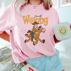 May include: A white ceramic mug with a black handle and the text "But First, Coffee" in a bold, black font. The mug is set against a blurred background, suggesting a cozy setting.