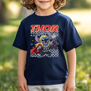May include: Navy blue t-shirt featuring a cartoon character as Thor, holding a hammer. The shirt has the text "Thor Stitch" in red and yellow. The character is on a checkered background with stars.