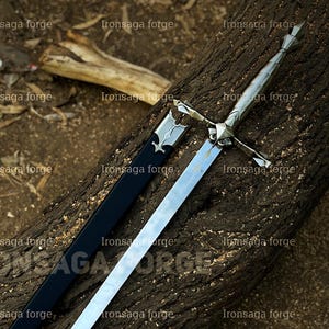 May include: A long, silver sword with a cross-shaped hilt and a black sheath rests on a weathered log. The sword's blade is polished, reflecting light. The text "Ironsaga forge" is visible in the image.