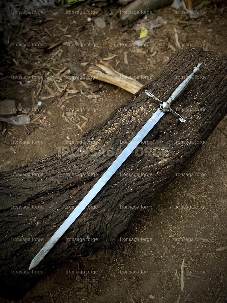 K&ouml;nnte beinhalten: Ein langes, silbernes Schwert mit kreuzf&ouml;rmigem Knauf liegt auf einem verwitterten, dunkelbraunen Baumstamm. Die Klinge ist gerade und poliert und reflektiert das Licht. Der Knauf des Schwertes weist komplizierte Details auf. Der Hintergrund ist nat&uuml;rlich und erdig.