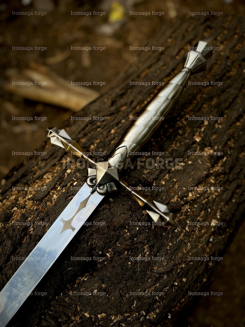 K&ouml;nnte beinhalten: Ein silbernes Schwert mit kreuzf&ouml;rmigem Knauf und langer, reflektierender Klinge. Das Schwert liegt auf einer dunkelbraunen, strukturierten Holzoberfl&auml;che. Die Klinge hat ein ge&auml;tztes Dekor.