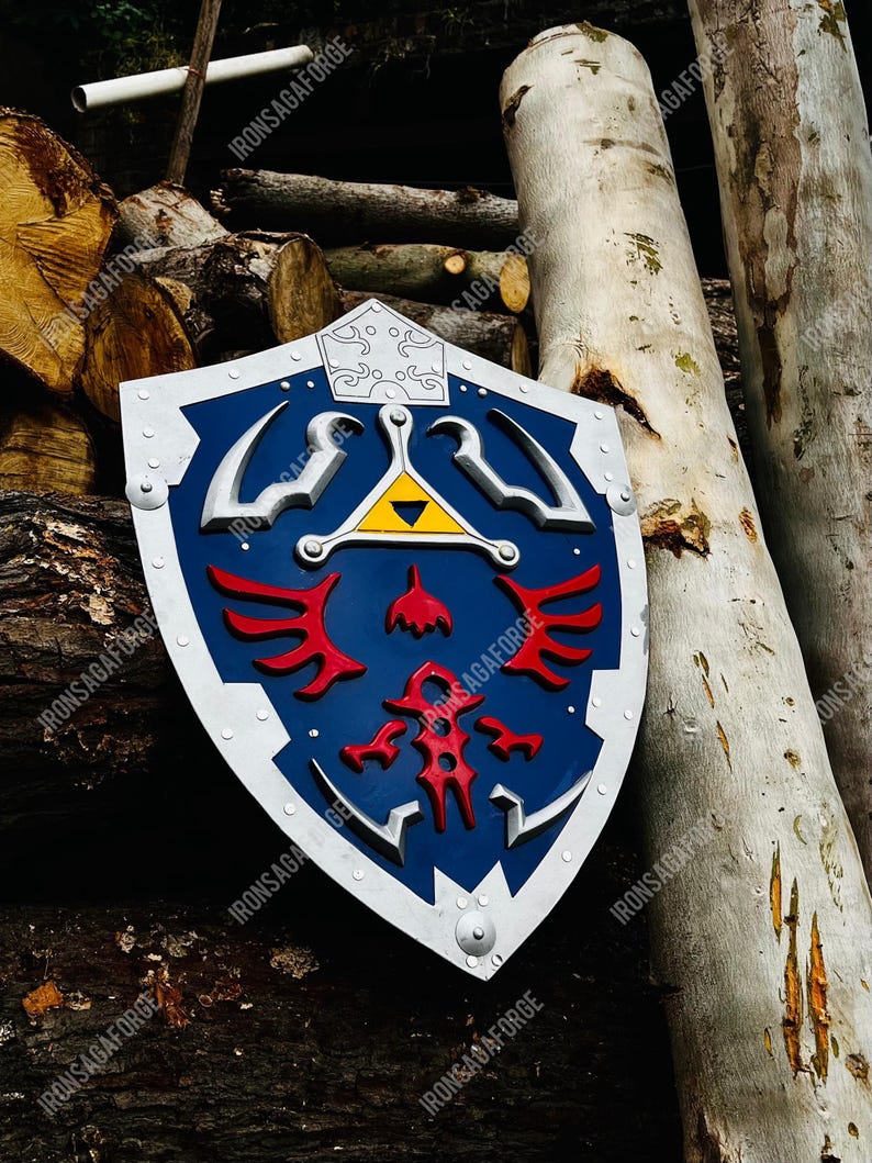 May include: A blue, white, and red shield with a silver trim and rivets. The shield features a central yellow triangle and red emblem. The shield is leaning against a pile of logs and tree trunks.