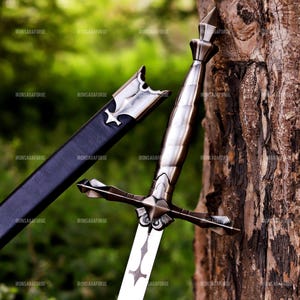 May include: A medieval-style sword with a silver blade and ornate hilt, next to a black sheath. The sword has a cross-shaped design on the blade and hilt. The background is a blurred green and brown, with the text "IRONSAGAFORGE" repeated.