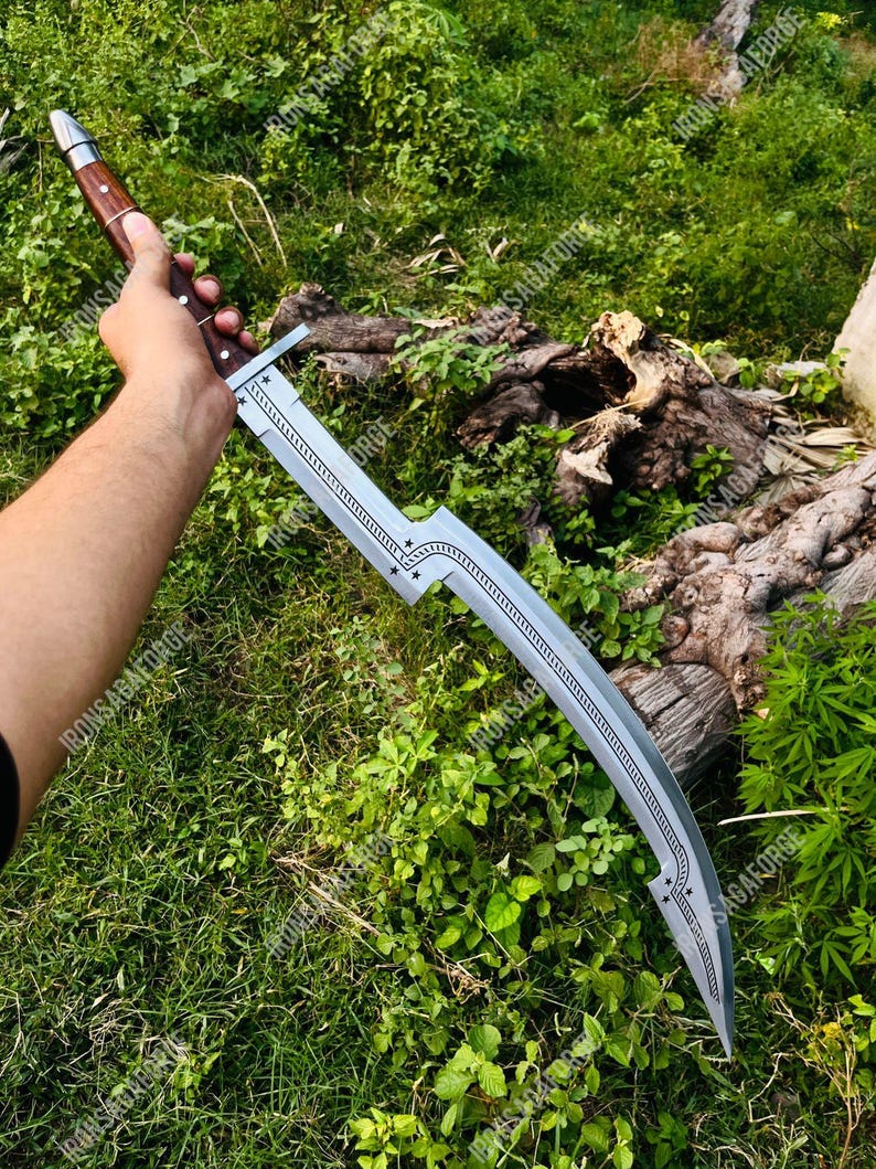 May include: A curved, silver blade sword with a wooden handle. The blade has decorative star-shaped cutouts and a detailed pattern along the spine. The handle is a dark brown color with silver rivets. The sword is held against a backdrop of green grass and foliage.