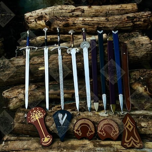 May include: A collection of swords, sheaths, and decorative shields are displayed on a wooden surface. The swords have various handle designs and blade styles. The sheaths are in different colors, and the shields feature intricate patterns and symbols.