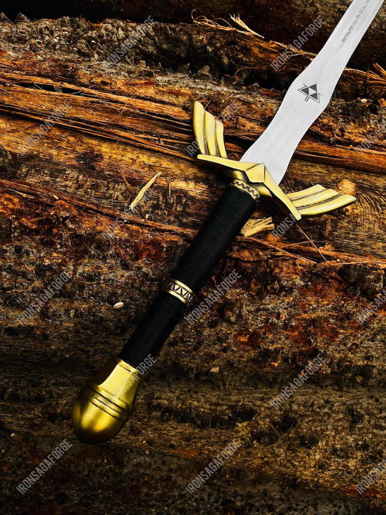 May include: A decorative sword with a silver blade and gold-colored hilt. The hilt features a black wrapped handle and gold accents. The sword is displayed on a wooden surface.