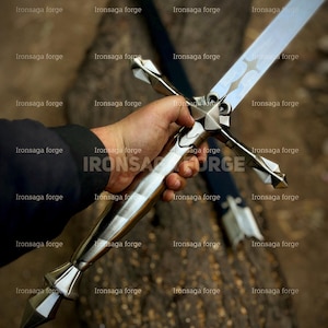 K&ouml;nnte beinhalten: Ein silbernes Schwert mit kreuzf&ouml;rmigem Knauf wird gehalten. Die lange, reflektierende Klinge hat eine Hohlkehle. Der Knauf hat ein Sterndesign. Der Text "Ironsaga forge" ist als Wasserzeichen zu sehen. Die Gesamtl&auml;nge des Schwertes betr&auml;gt ca. 76 cm.